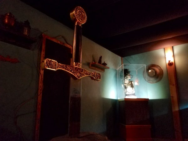 The hilt of a sword in the foreground, with museum pieces including a bust under glass in the background.