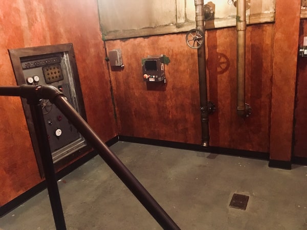 In-game: a weathered space with tubes and controls.