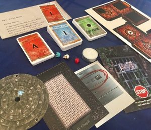 In-game: An assortment of card decks, paper props, a tea candle, and multicolored skulls.