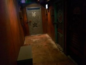 In-game: A long hallway with a door painted like a jigsaw puzzle at the end of it.