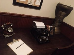 In-game: A desk with an old typewriter, a book, a phone, and an ancient egyptian artifact.