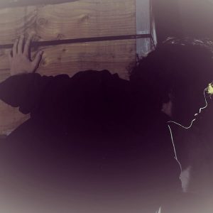 In-game: A person sneaking around a wooden crage in a dark room.