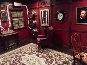 In-game: a red abd brown study with a large electrical contraption. Bulky wires emerge from it.