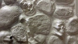 A white vacuform panel that looks like a mistrure of stones and skulls sealed with mortar to make a wall.