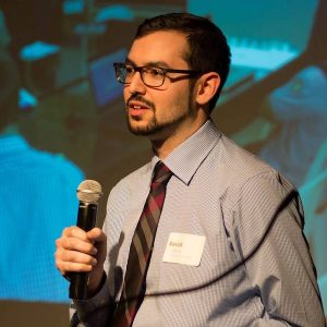 David holding a microphone and delivering a talk on a stage.