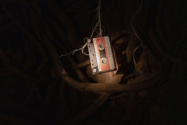 Light shines on a cassette tape dangling from a piece of twine in front of a background of tree roots.