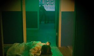 In-game: a dead body on the floor in the foreground, a zombie lurking in the background.