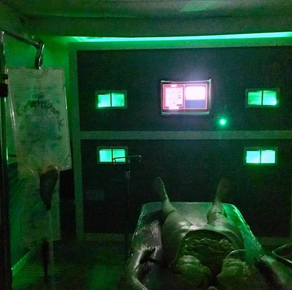 In-game: A dead person on an operating table in a green lit room, their organs are exposed.