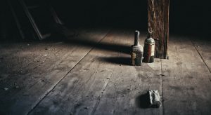 A dirty, dusty, dark room with a pair of old and open liquor bottles casting long shadows.