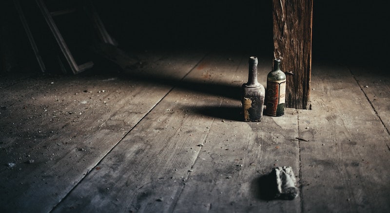 A dirty, dusty, dark room with a pair of old and open liquor bottles casting long shadows.