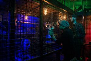 In-game: Two people looking into a caged area and some strange artifacts.