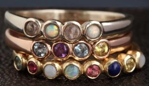 A stack of three rings in silver, gold, and rose gold. Each has a different arrangement of stones on the band.