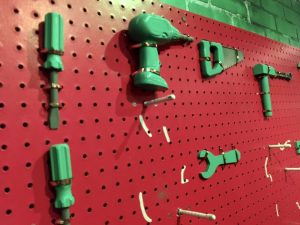 In-game: a red pegboard with green toy tools hanging from it.