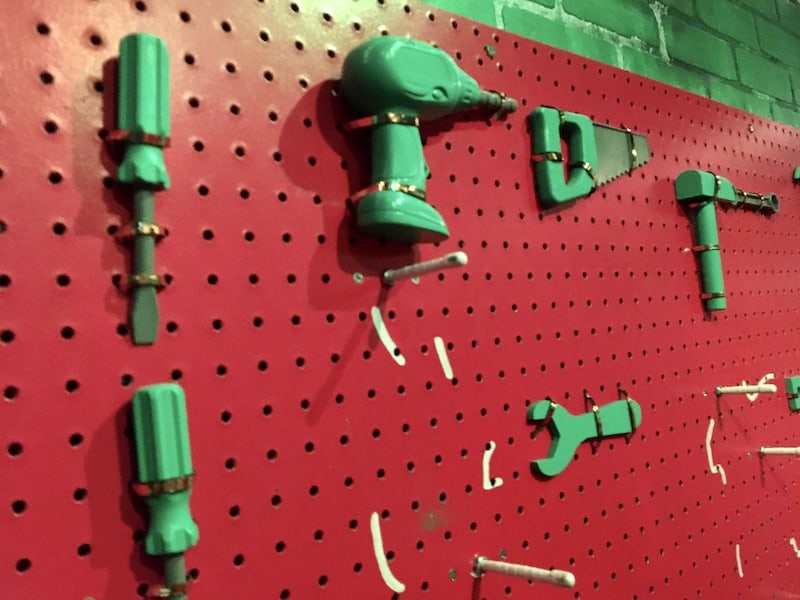 In-game: a red pegboard with green toy tools hanging from it.