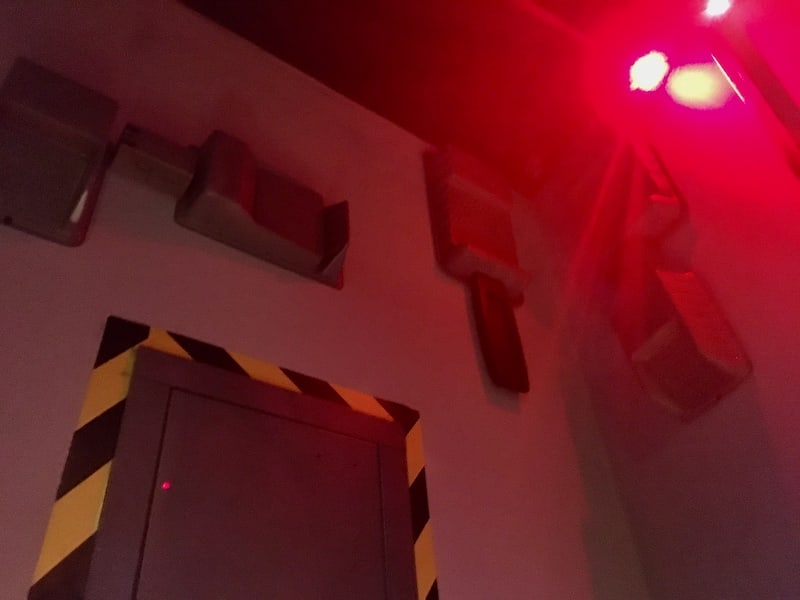 In-game: An assortment of wallmounted machinery and a flashing red alarm light.