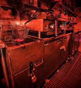 In-game: A red tinged view of an restaurant kitchen.