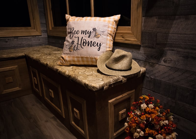 In-game: A corner bench seat with a pillow that reads, "Bee my honey" depicting two bees.