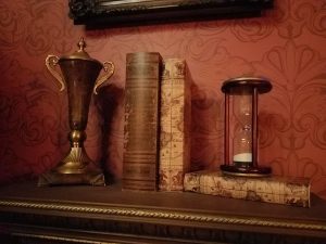 A trophy, an hourglass, and some books sit on an ornate shelf.