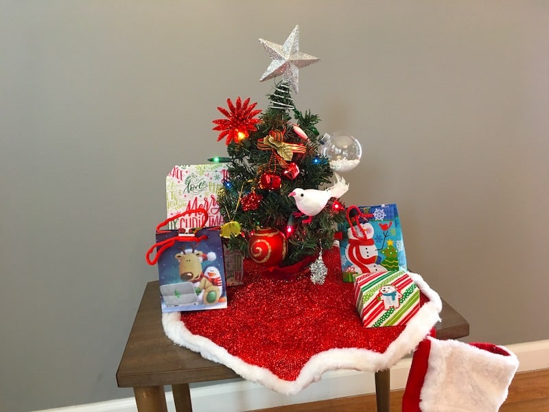 A tiny christmas tree with gifts gathered around it on a small table.
