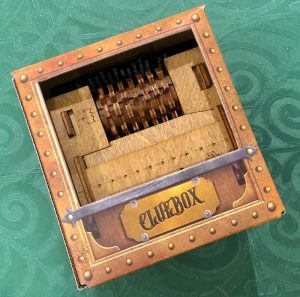 A wooden puzzle box inside of its cardboard packaging labeled, "Cluebox."