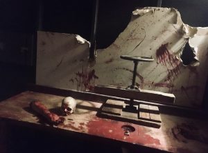 In-game: A table covered in blood, body parts, and a large clamp.