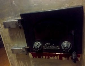 In-game: closeup of an incinerator door, blood runs out from under it.