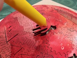 A pen with a sticky tip being used to extract a piece shaped like an alien from the assembled puzzle.