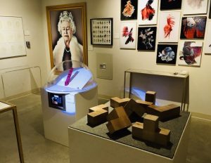 In-game: Wide view of the gallery, many pieces are on display, the two most prominent is a painting of the Queen of England with her eyes closed.