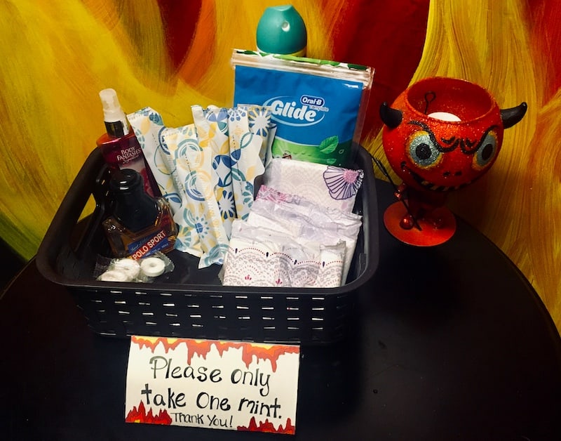 A basket with floss, maxipads, tampons, mouthwash, and mints in a bathroom.