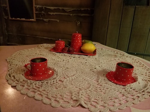 Teacups, candles, and fruit on a doily-covered table.