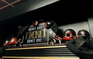 In-game: an "Admit One Ticket" sign flanked by freaky baby doll parts pained black and red.