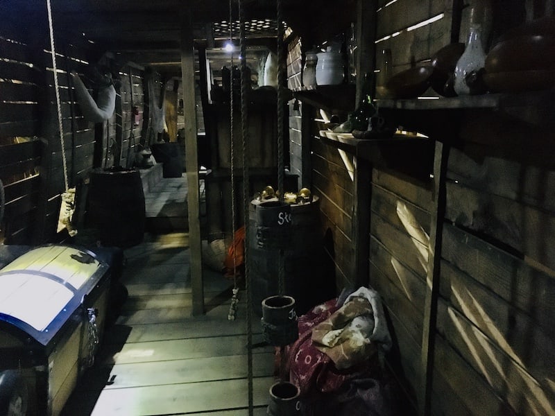 In-game: A view through a long, old, wood ship. A treasure chest sits on the floor.