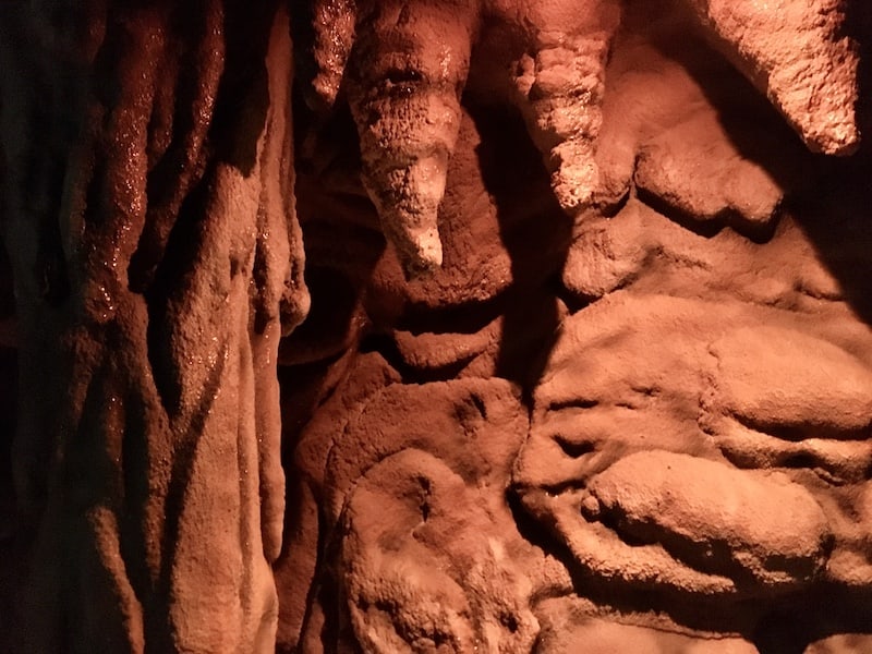 In-game: stalactites hanging from a red walled of a cave.