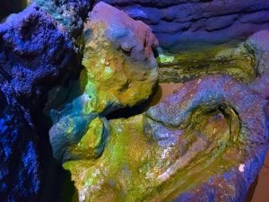 In-game: closeup of an effervescent blue and yellow rock structure with water running through it.