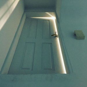 A mysterious door high up on a wall. It's cracked open with light passing through the crack.