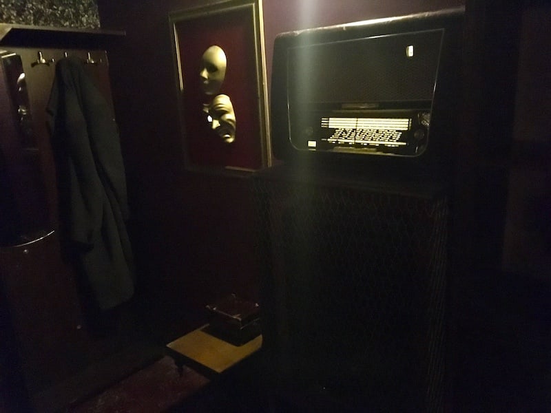 In-game: The corner of a home, with a radio, and comedy and tragedy masks.