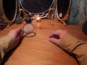 Hands of a detective holding magnifying glass on a table set with mysterious objects.