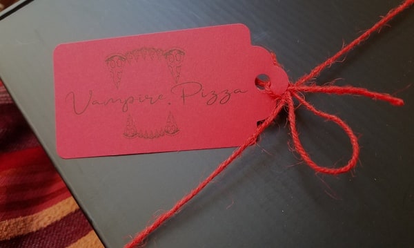 A tag reading "Vampire Pizza" tied to a black box with red twine.