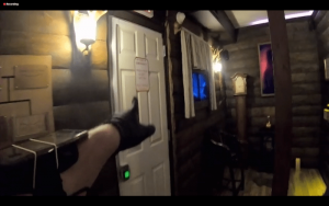 A black gloved hand pointing at a door inside of a cabin.