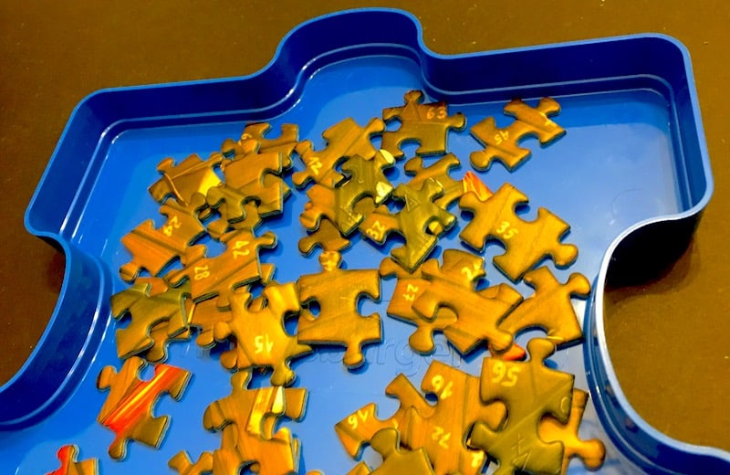 Traditional cardboard jigsaw puzzl pieces in a tray shaped like a blue puzzle piece.