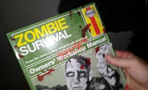 First person of a hand holding a Zombie Survival guidebook.