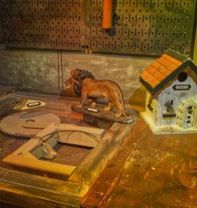Zoom view of a workbench with a model house, a statue of a lion, and a strange mechanical contraption.