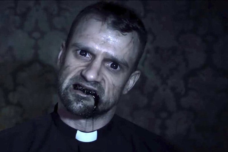 A posessed priest with black fluid flowing from his mouth and dead eyes.