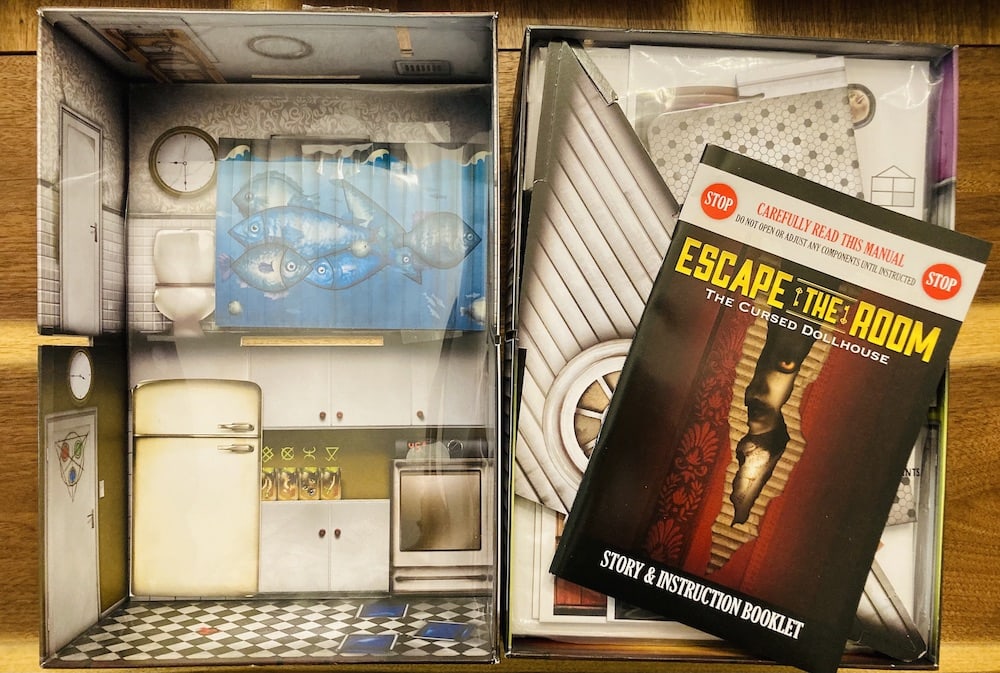 Box opening shows a kitched and bathroom, assorted cardboard piececs, and an instruction booklet.