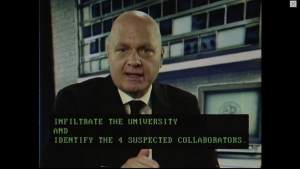 A bald man looking into the camera, briefing the team.