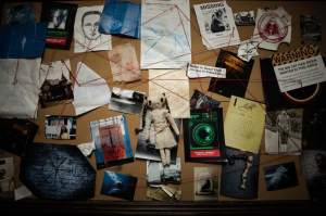 A bulletin board covered in documents, photos, and red string.