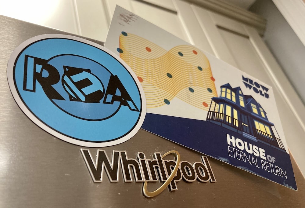 REA magnet holding up a postcard from Meow Wolf