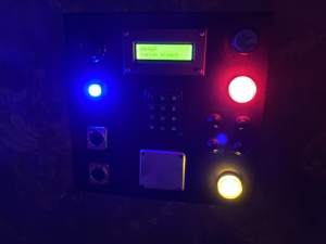 In-game: closeup of a panel with a keypad, many glowing lights, and a display that reads, "Danger: System breach."