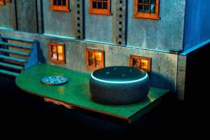 An Alexa Dot sitting beside the dollhouse.