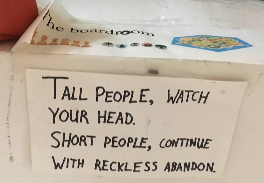 A sign hung under a low doorway reads, "Tall people, watch your head. Short peopel, continue with reckless abandon."
